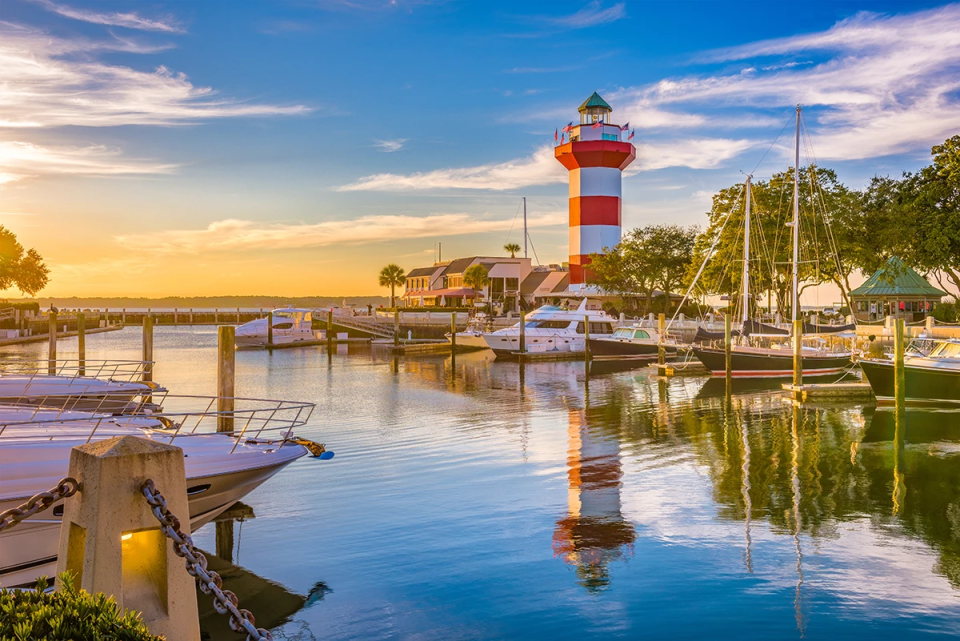 Hilton Head Island sunset over the water with a lighthouse, boats, and a bridge in the background.